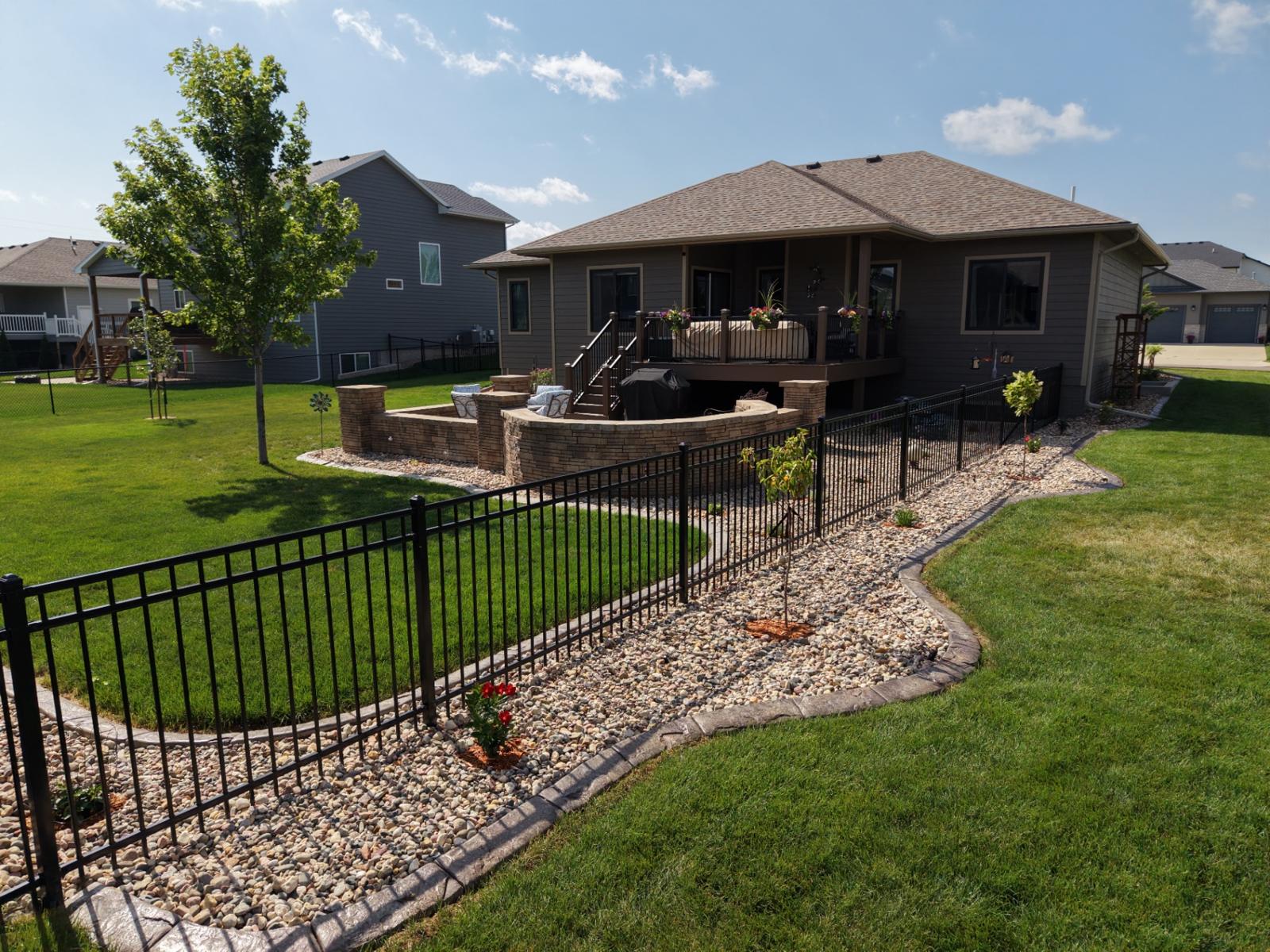 Drone view of a finished Sioux Falls backyard landscape with stamped patio, fire pit, and river rock beds