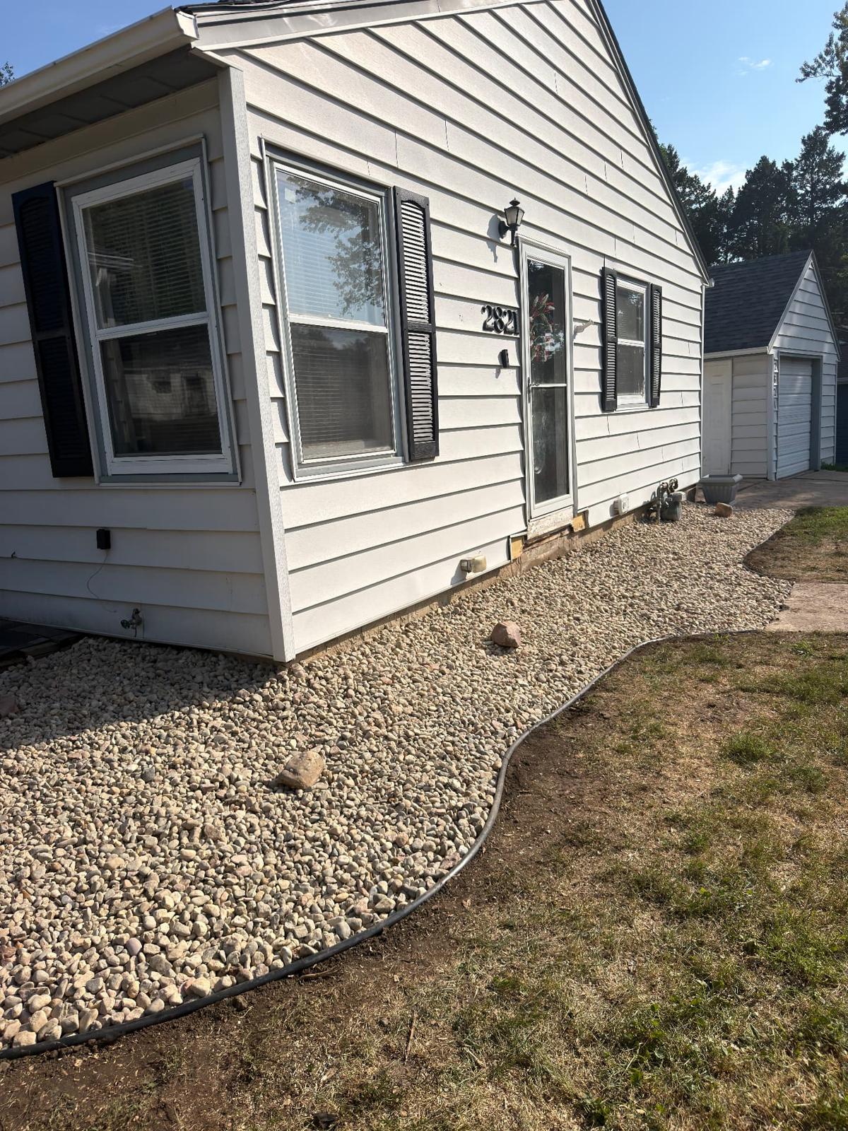 After — regraded front landscape bed in clean river rock with new plastic edging wrapping the side entry of a white sided home in Sioux Falls