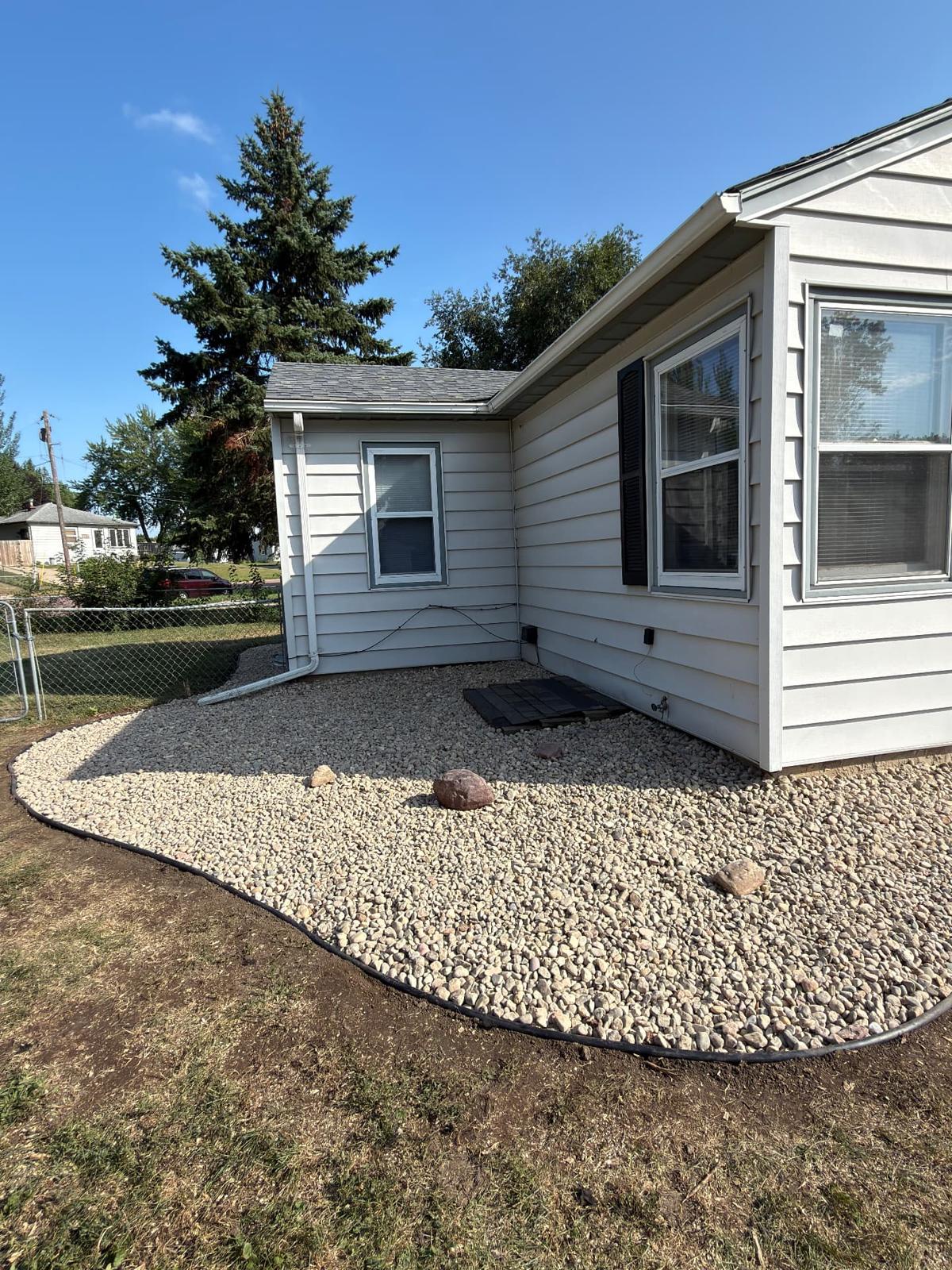 After — wide river rock landscape bed with accent boulders and crisp edging, regraded to shed water away from the foundation