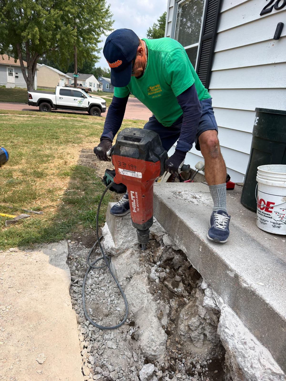 During — Kerwin Property Maintenance crew member breaking out the old front concrete steps with a Hilti breaker to prep for the new deck