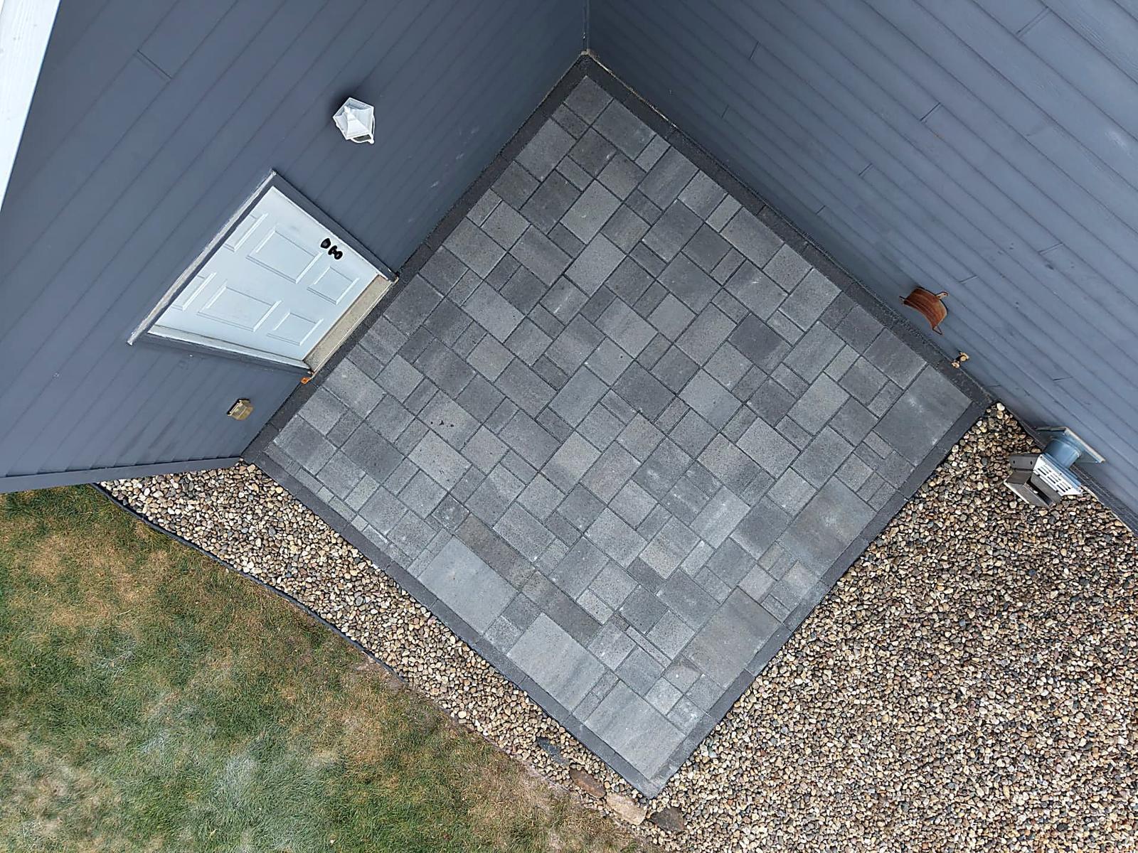 After — top-down drone view of the custom 12x12 paver patio showing the tight random-pattern layout and charcoal soldier-course border