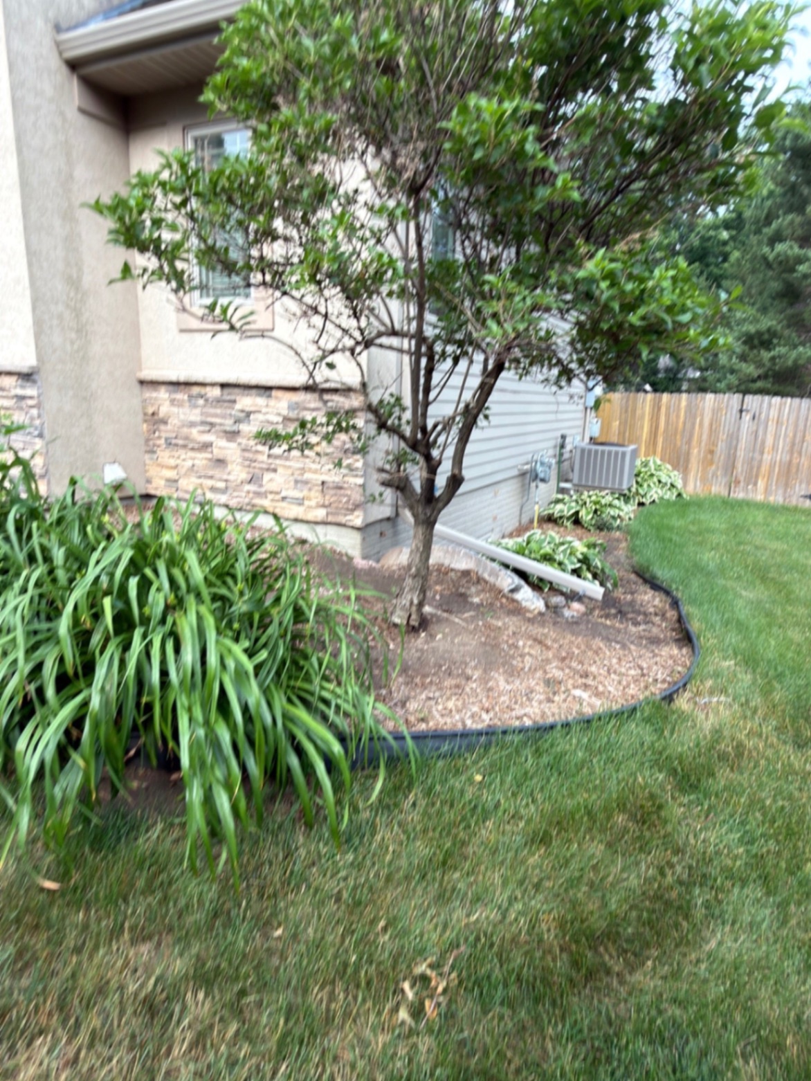 Before — side bed by the stone-accented home with old mulch, daylilies, and a shrub before the rock refresh