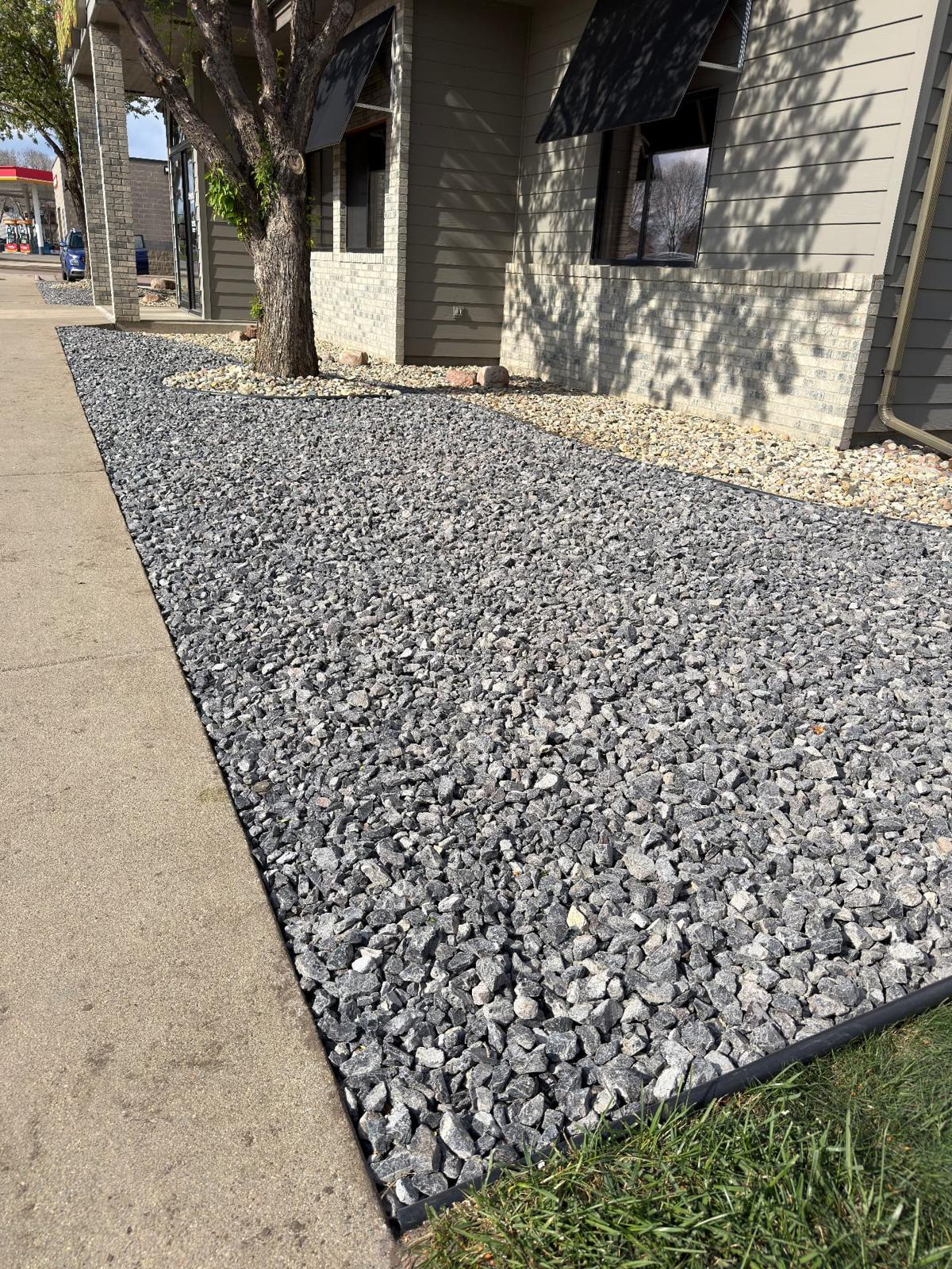 After — charcoal crushed rock bed with clean plastic edging running the length of a commercial building walkway in Sioux Falls, SD