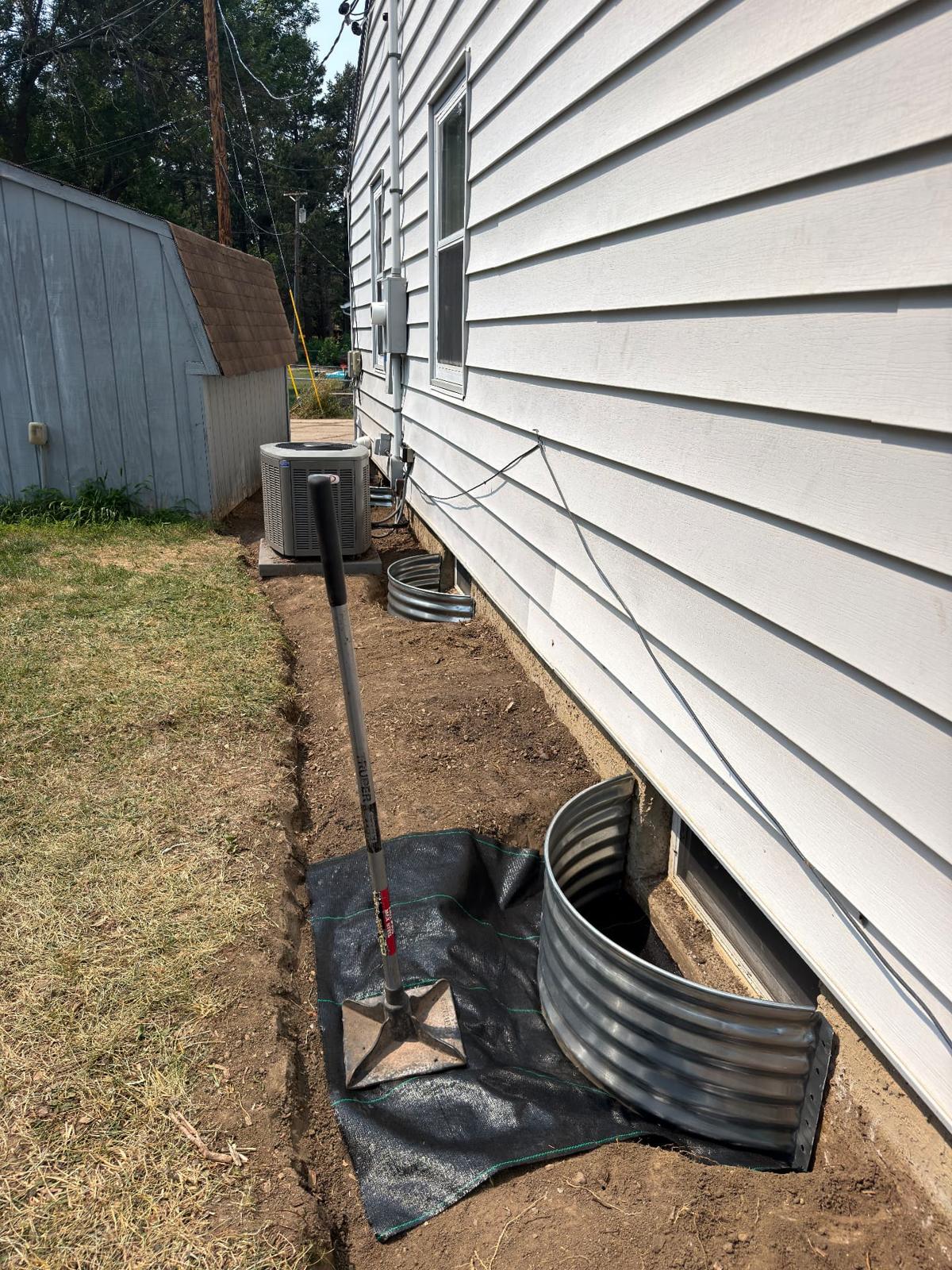 During — new galvanized window wells set in place with weed fabric laid over the regraded trench before gravel and river rock