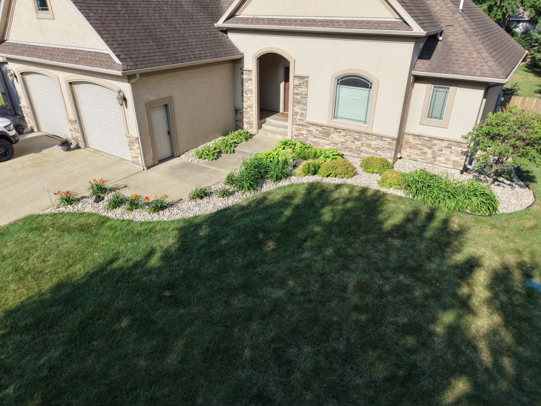 After — front entry beds with daylilies and shrubs in river rock around stone-accented home