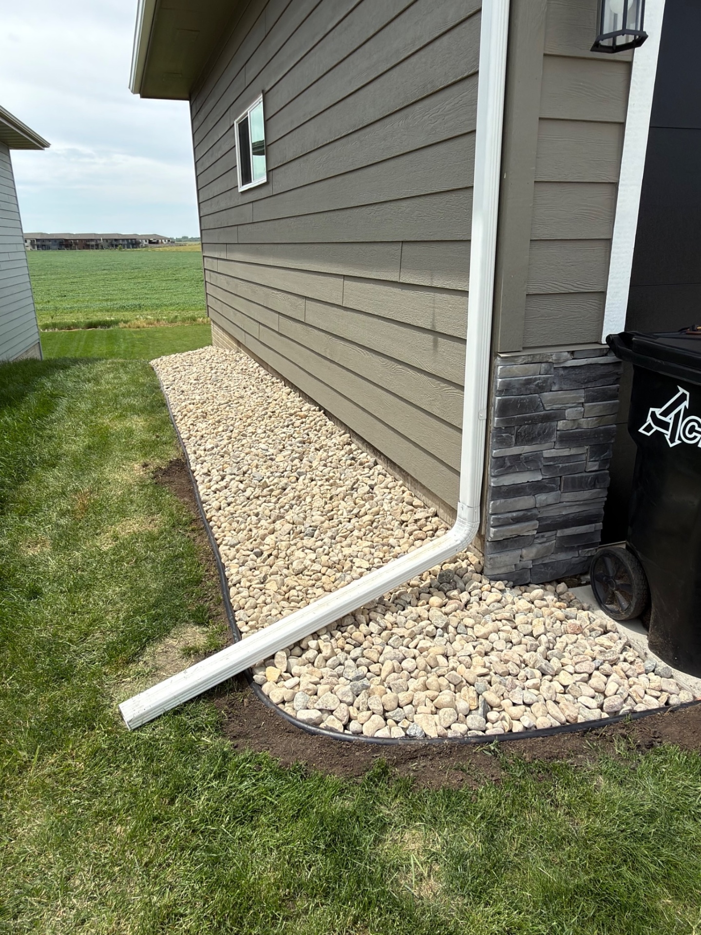 After — finished rock bed around the downspout and corner of the house with stone column accent and tidy edging