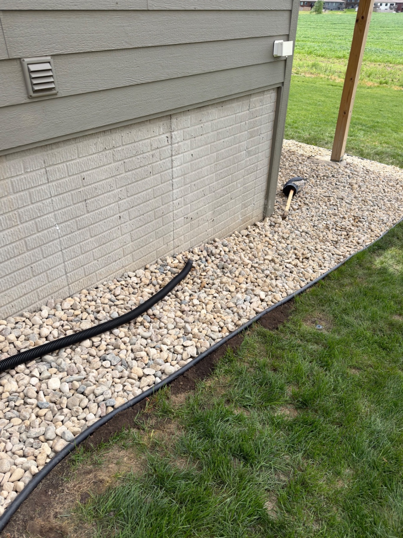 After — finished river rock bed along the foundation with french drain line and clean steel edging against the grass