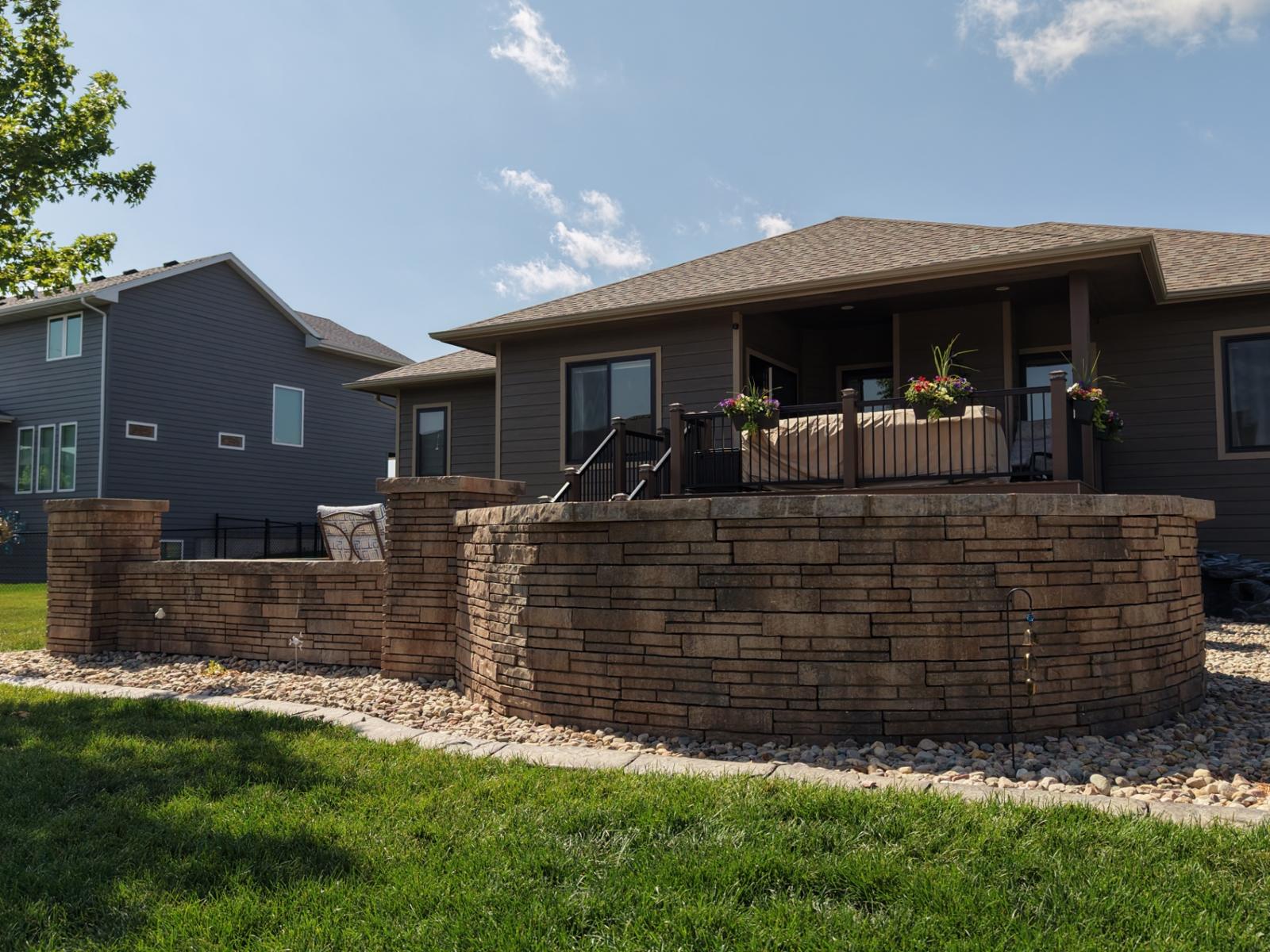 Curved stacked-stone seat wall wrapping an elevated deck with river rock beds in Sioux Falls, SD