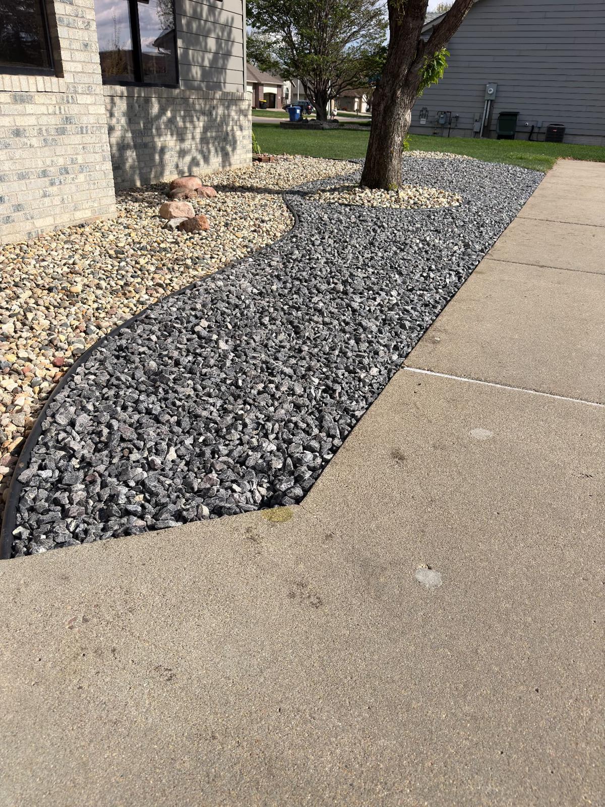 After — two-tone rock blend with charcoal crushed rock and tan river rock separated by curved edging around a shade tree