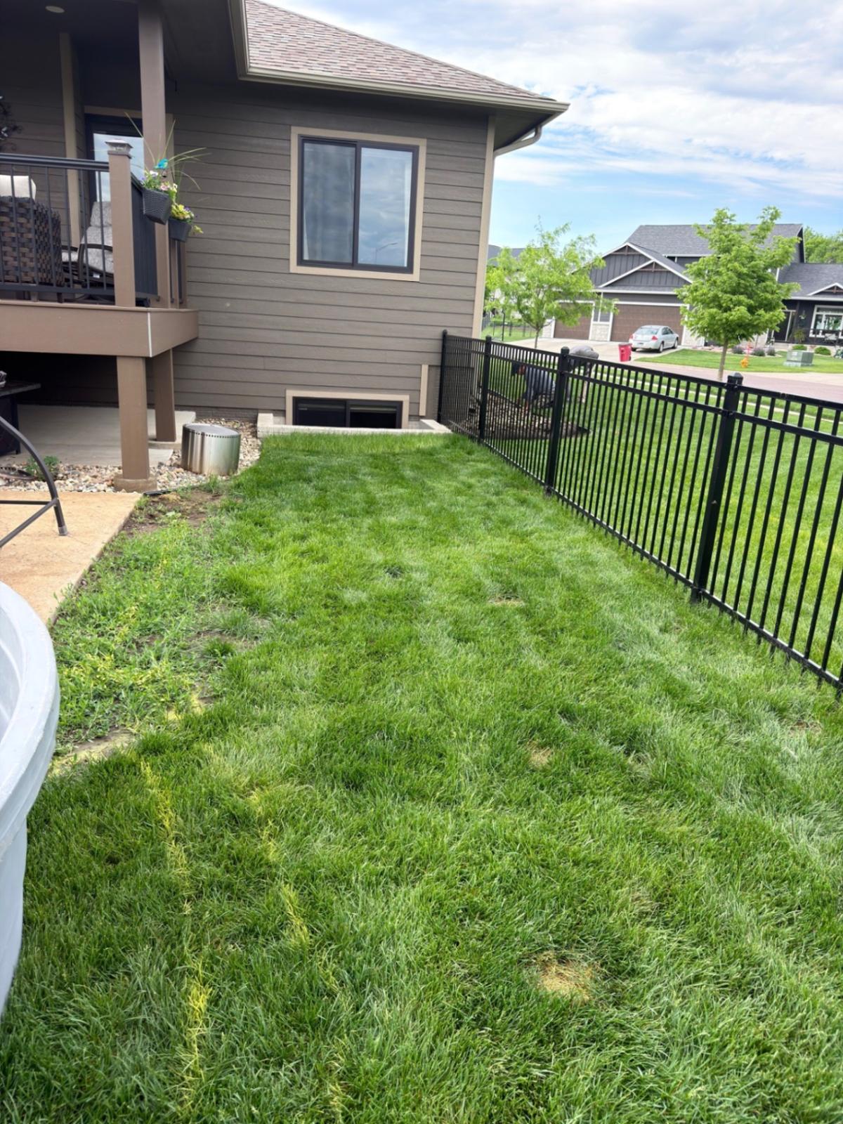 Before — narrow side yard strip with patchy grass along the deck and iron fence before the landscape extension