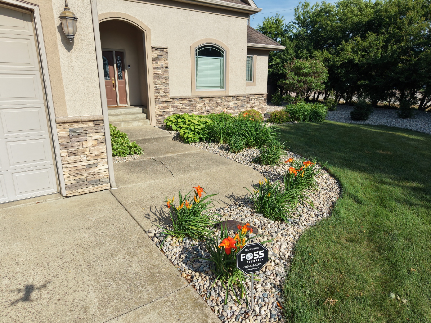 After — drone view of front entry walkway with river rock beds, daylilies, and crisp edging against a healthy green lawn