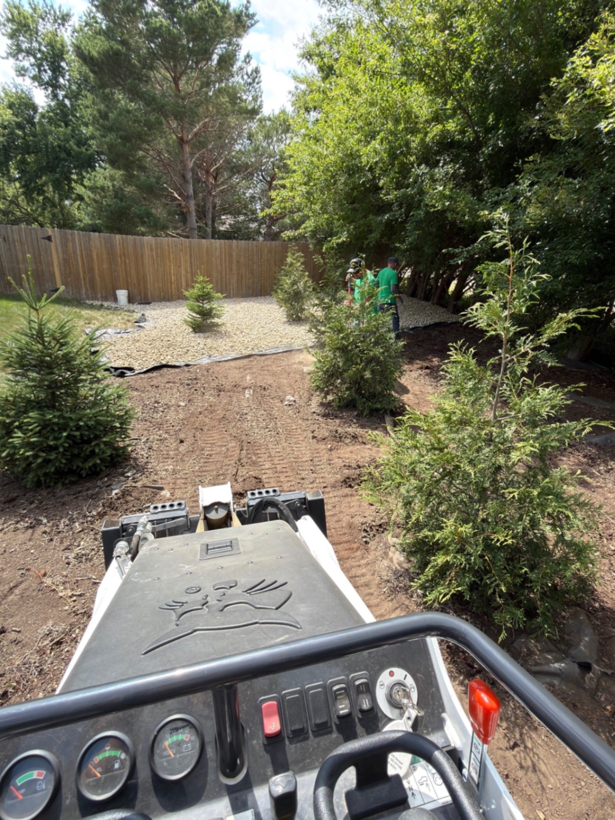 During — operator's view from the Bobcat mini skid steer grading the backyard with rock beds taking shape between the trees