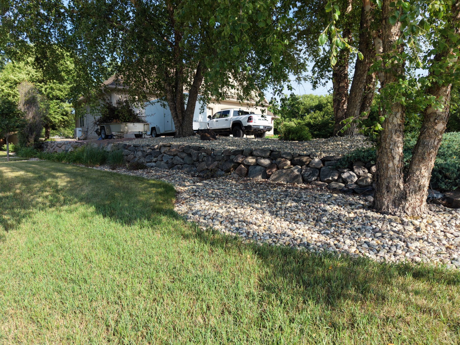 After — natural stacked boulder retaining wall holding back an elevated river rock yard under mature trees