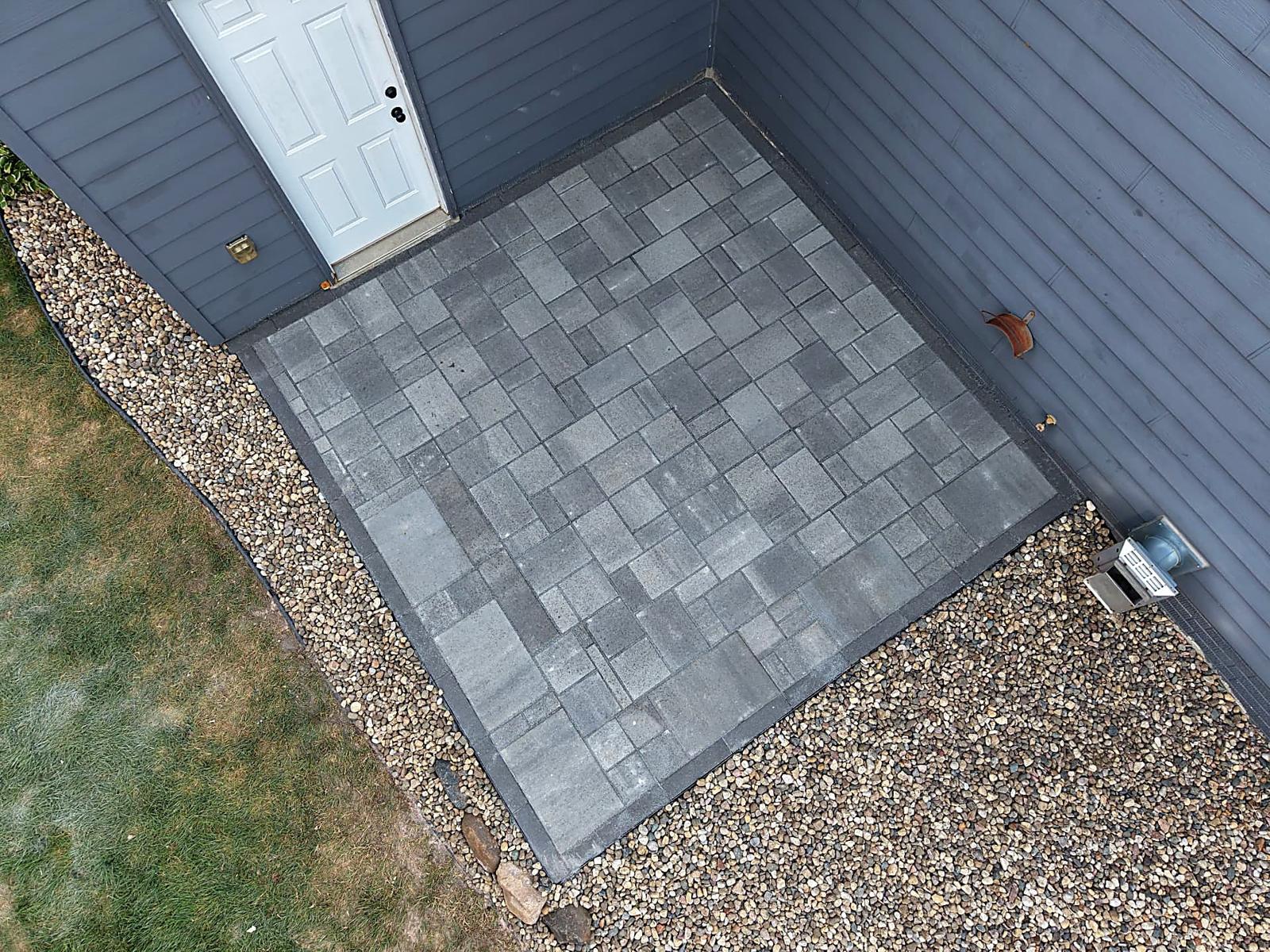 After — aerial angle of the completed 12x12 patio with shortened side bed and crisp edging between the rock and lawn