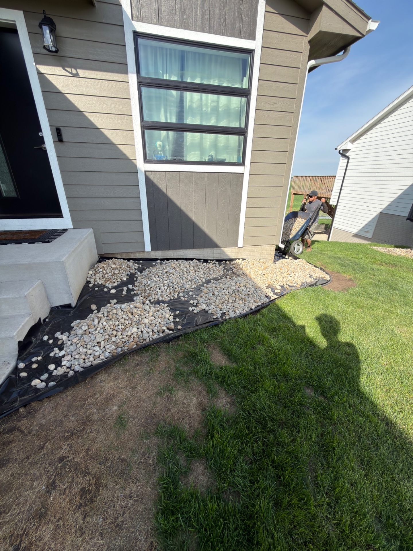During — Edging laid along the side of the house with river rock being spread by wheelbarrow