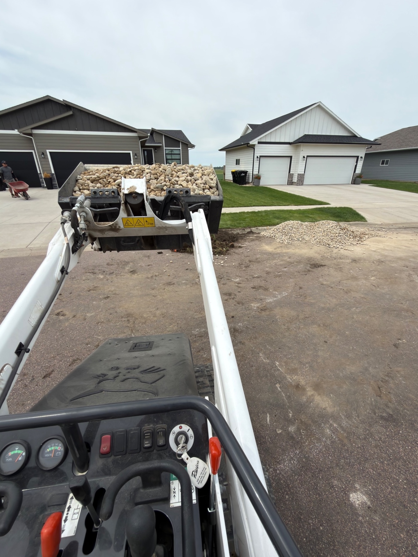 During — operator's view from the Bobcat hauling a bucket full of river rock down the driveway