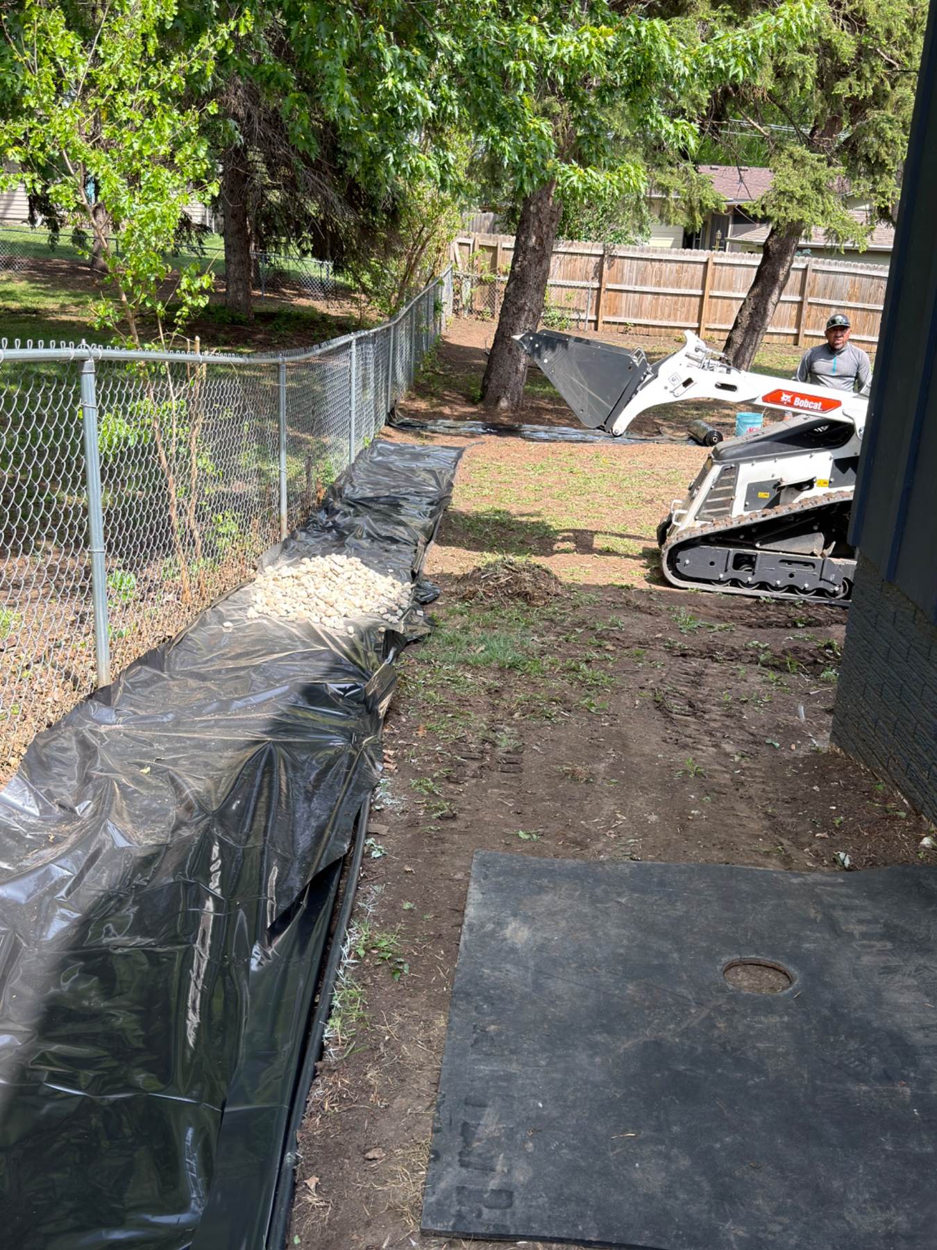 During — Bobcat mini skid steer grading the yard with rock bed taking shape along the fence