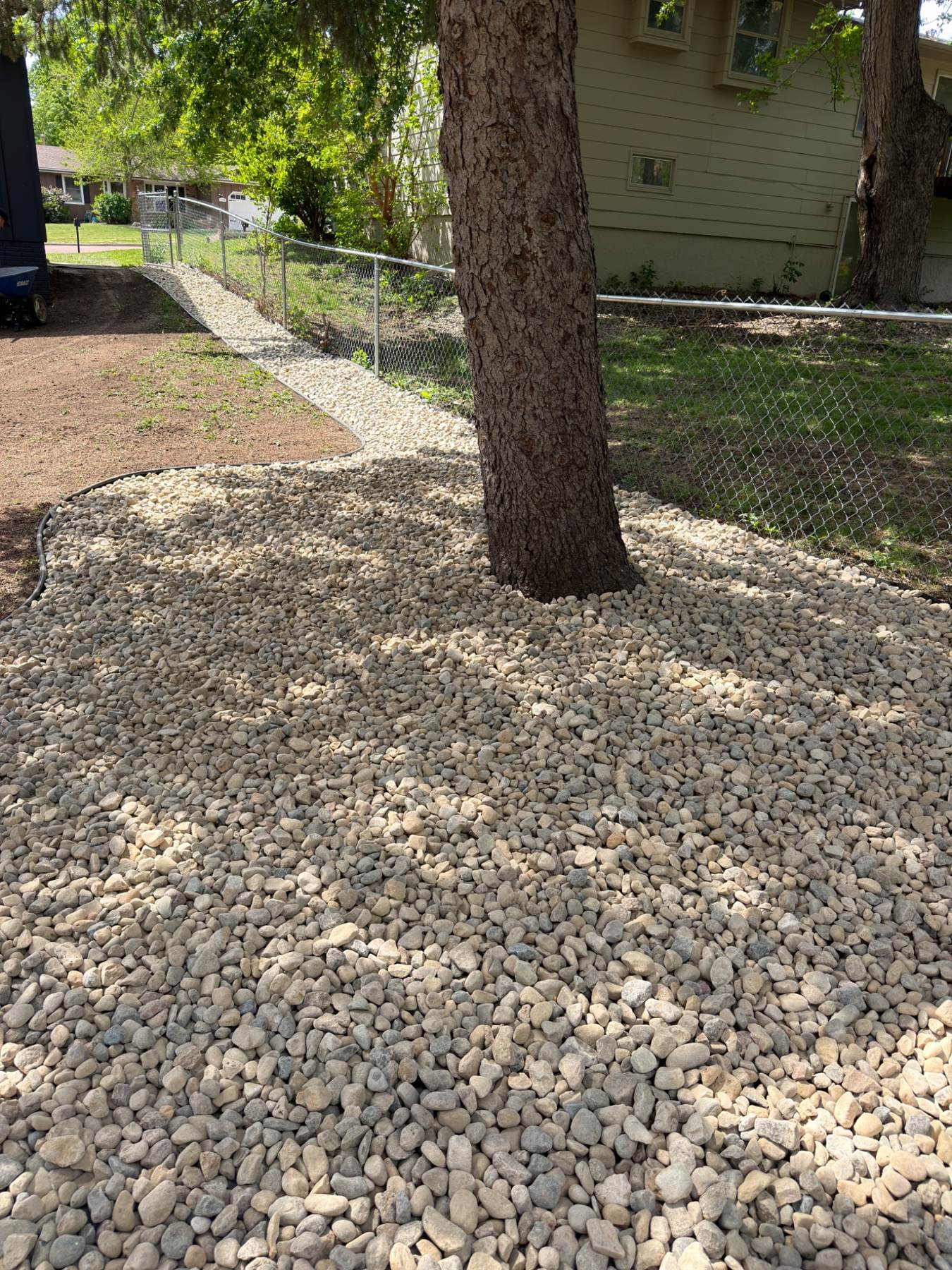 After — finished rock landscaping bed wrapping a mature tree along the side yard